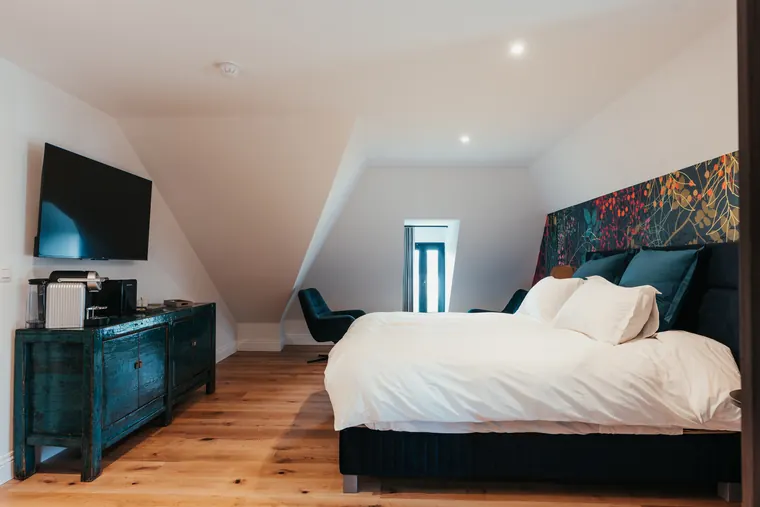 Suite Elite — vue d'ensemble : lit king face à la télévision, commode en bois patiné et fauteuils près de la fenêtre