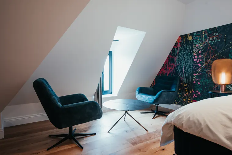 Suite Elite — coin salon sous les combles : deux fauteuils en velours bleu et table basse baignés de lumière